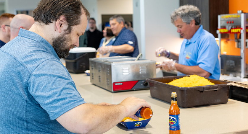 LCS employees eating a company provided lunch at the office. A man is eating a cheese coneys from Skyline Chill. 